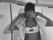Model undoes hooded coat to reveal bra top; 1970