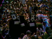 Zoom out from crowds of people at anti-war demonstration&sbquo;  3 people in large death mask costumes labelled Cambodia&sbquo; Laos&sbquo; Vietnam&sbquo; Washington DC; 1970s