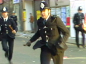 Pan left as four police officers with truncheons avoid objects being thrown and chase young man through crowded street during riots&sbquo;  Brixton; Apr 81